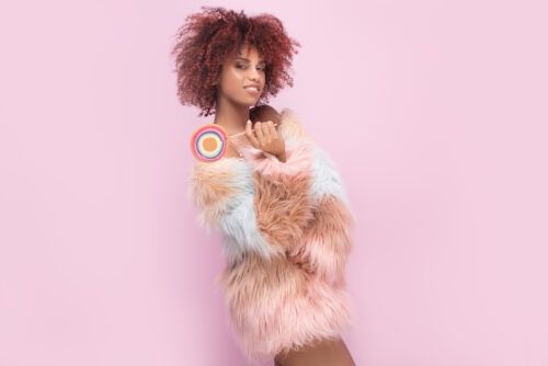 Mulher afro elegante com pirulito em fundo rosa grata pelo anjo número 4242
