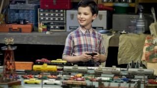Serie de televisión Young Sheldon: Un niño con una camisa a cuadros sonríe mientras sostiene el controlador de un tren en miniatura.