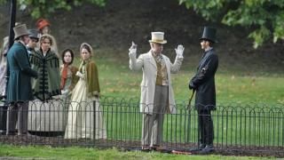 Serie Good Omens: Crowley y Aziraphale tienen una discusión sobre ropa victoriana de época frente a una pequeña multitud de personas vestidas con ropa similar