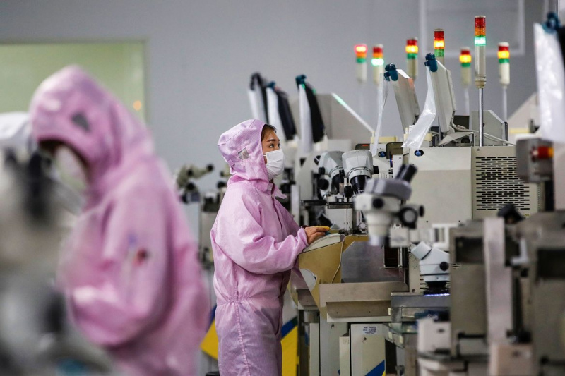 Kinijos darbuotojai, dėvintys veido kaukes ir apsauginius kostiumus, dirba išmaniosios mikroschemų gamybos linijoje