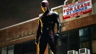 Мужчина в черно-красном кожаном костюме супергероя стоит на крыше перед вывеской «Продается здание».