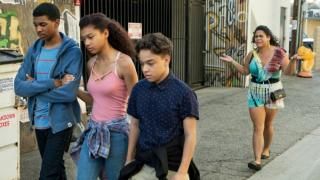 Трима тийнейджъри минават по изпъстрена с графити градска улица, докато друго момиче върви леко зад тях и крещи нещо по тях.
