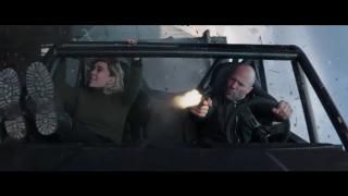 Fast & Furious presenta la película de Hobbs & Shaw: Shaw conduce y dispara un arma mientras Hattie sonríe desde el asiento del pasajero, escombros de explosión en el fondo